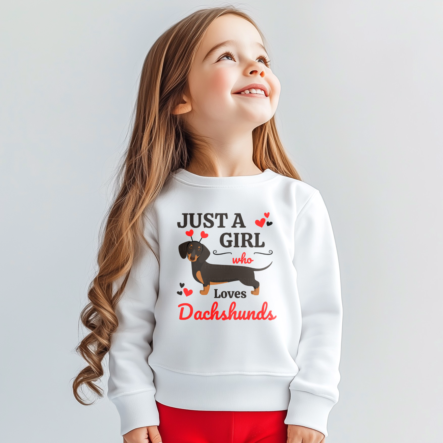 A young girl models a white “Just a Girl Who Loves Dachshunds” sweatshirt with cute dachshund and red hearts graphic