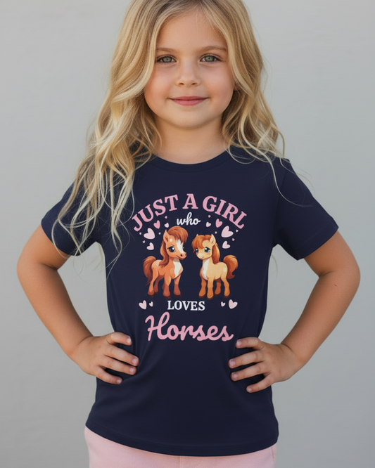 Blonde young girl modelling a navy “Just A Girl Who Loves Horses” kids t-shirt with pink lettering and cute pony graphic, hands on hips, studio background.