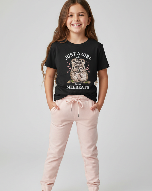 Smiling young girl wearing a black “Just a Girl Who Loves Meerkats” graphic t-shirt with pink joggers against a light studio background