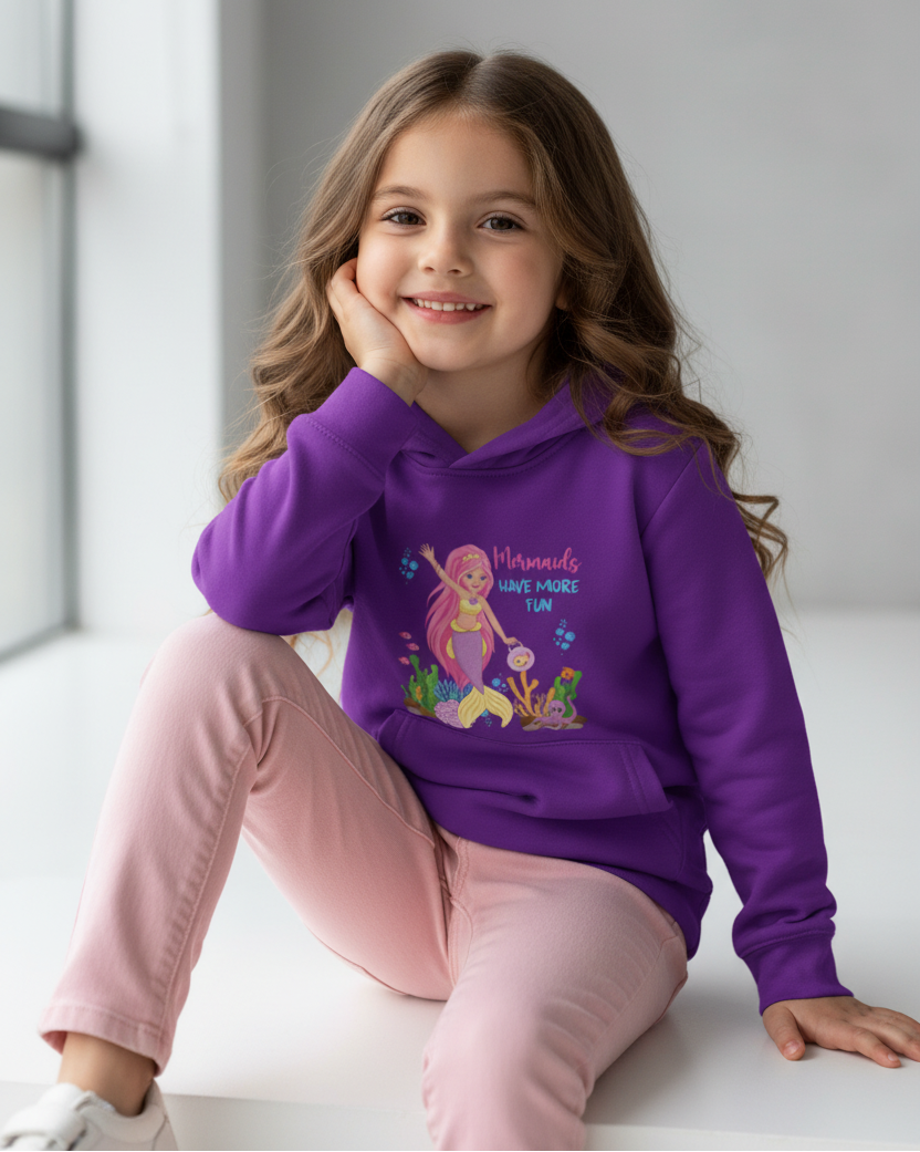 Smiling girl sitting in studio wearing purple “Mermaids Have More Fun” kids hoodie with ocean-themed print