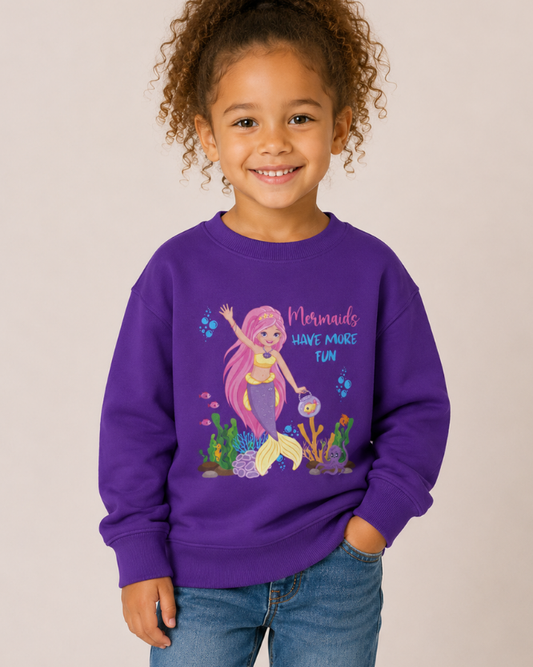 Young girl smiling wearing purple mermaid sweatshirt with “Mermaids Have More Fun” design in studio setting