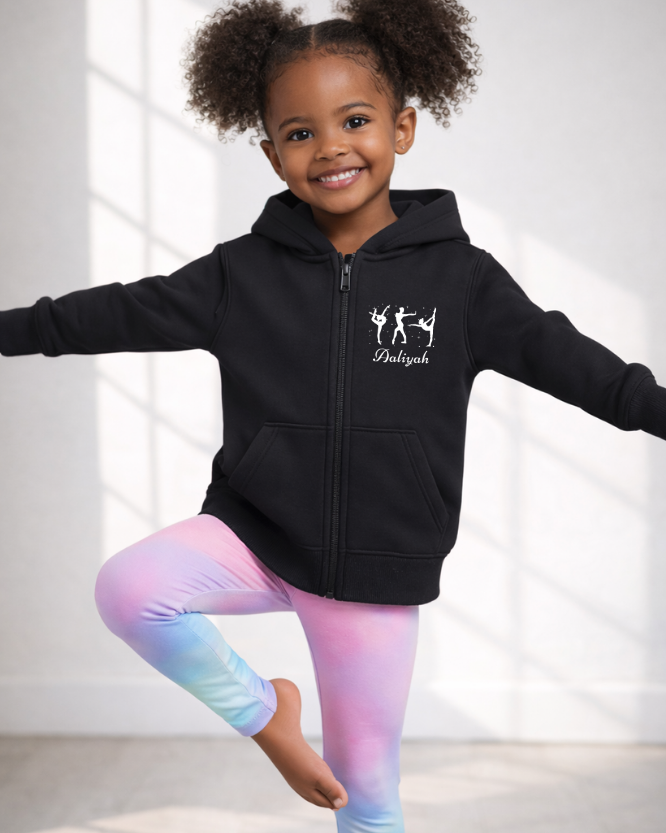 Young girl wearing personalised black gymnastics zip hoodie, balancing in a pose, name printed on chest.
