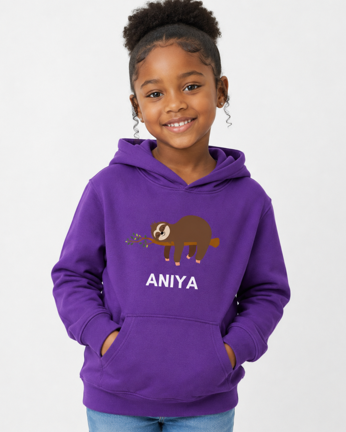 A young girl with her hair in a high bun is wearing a purple hoodie with a sleeping sloth graphic and the name 'ANIYA' printed in white. She is also wearing blue jeans, standing against a plain white background.