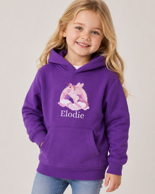 Girl wearing personalised purple unicorn kids hoodie with rainbow cloud print and custom name in studio setting