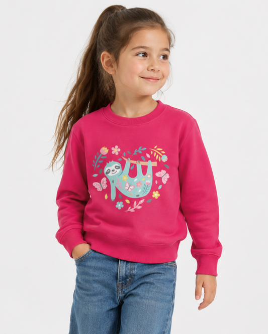 Happy young girl in a long ponytail wearing a bright pink kids sweatshirt with a pastel floral sloth heart graphic, styled with wide leg denim jeans in a bright studio hero image.