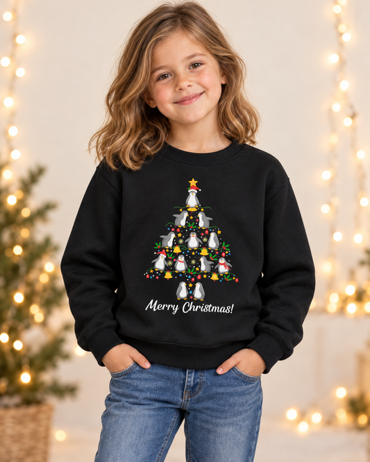 Young girl smiling while wearing a black Christmas crewneck sweatshirt featuring penguins stacked in a Christmas tree shape with festive ornaments and 'Merry Christmas!' written below