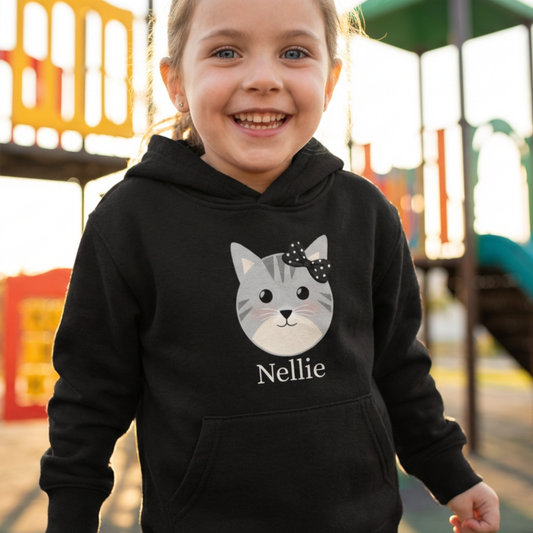 Little girl wearing a black hoodie with a cat graphic and 'Nellie' text on a playground background