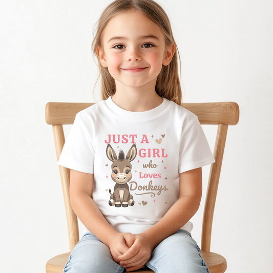 Young girl wearing a white t-shirt with a donkey graphic and text, sitting on a wooden chair.