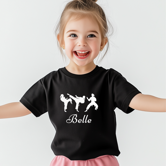 Little girl wearing a black martial arts t-shirt with three white karate silhouettes and a custom name printed underneath in script font