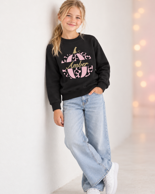 Blonde girl wearing a personalised black Halloween sweatshirt with a pink leopard-print pumpkin and the name Amber.