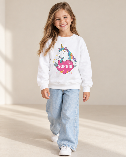 Girl wearing a white personalised unicorn sweatshirt with a rainbow mane, pink heart and the name Sophie, styled with wide-leg jeans.