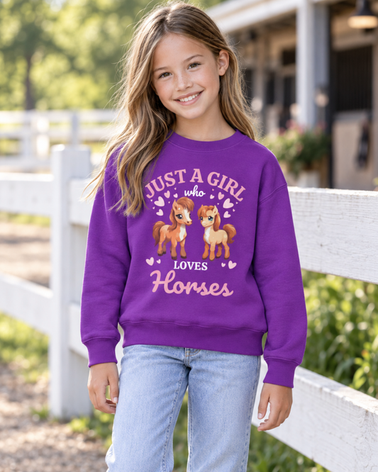 Girl wearing a purple Just a Girl Who Loves Horses sweatshirt featuring two illustrated horses and pink hearts beside a paddock fence.