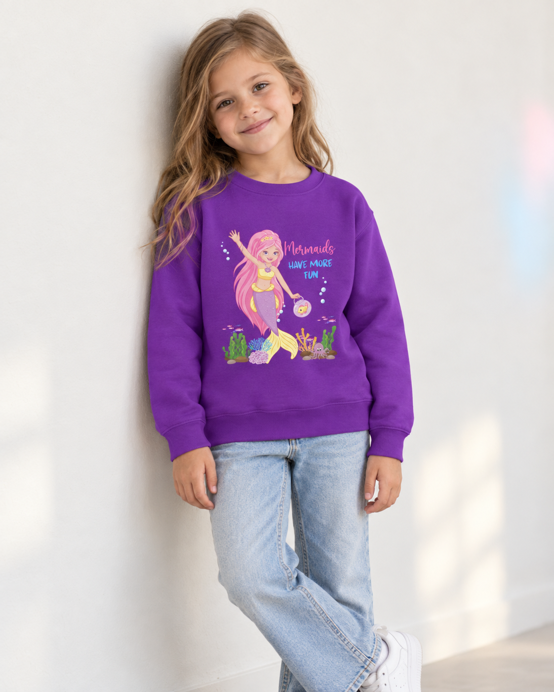 Girl wearing a purple Mermaids Have More Fun sweatshirt featuring a pink-haired mermaid, colourful coral and sea creatures.