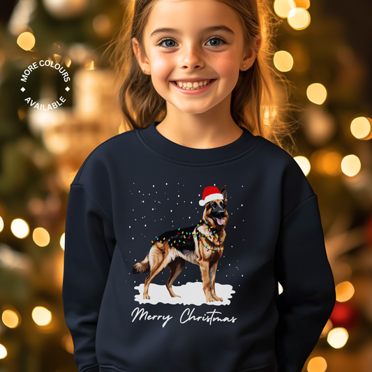 A child wearing a navy sweatshirt with a graphic of a German Shepherd dog wearing a Santa hat, surrounded by fairy lights, with the text 'Merry Christmas'.