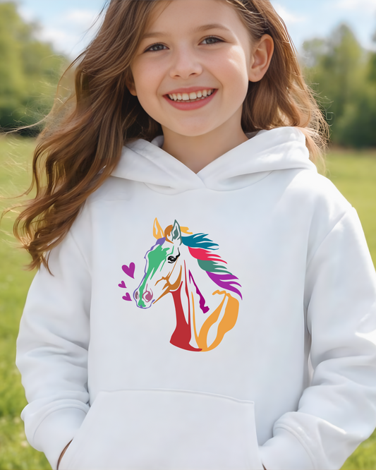Young girl wearing a white hoodie with a colorful horse design in a grassy field.