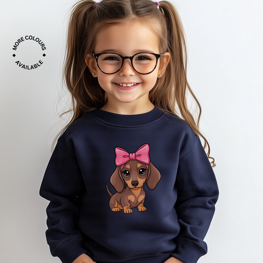 Young girl wears a navy sweatshirt with a cute dachshund illustration featuring a large pink bow, coquette aesthetic style.