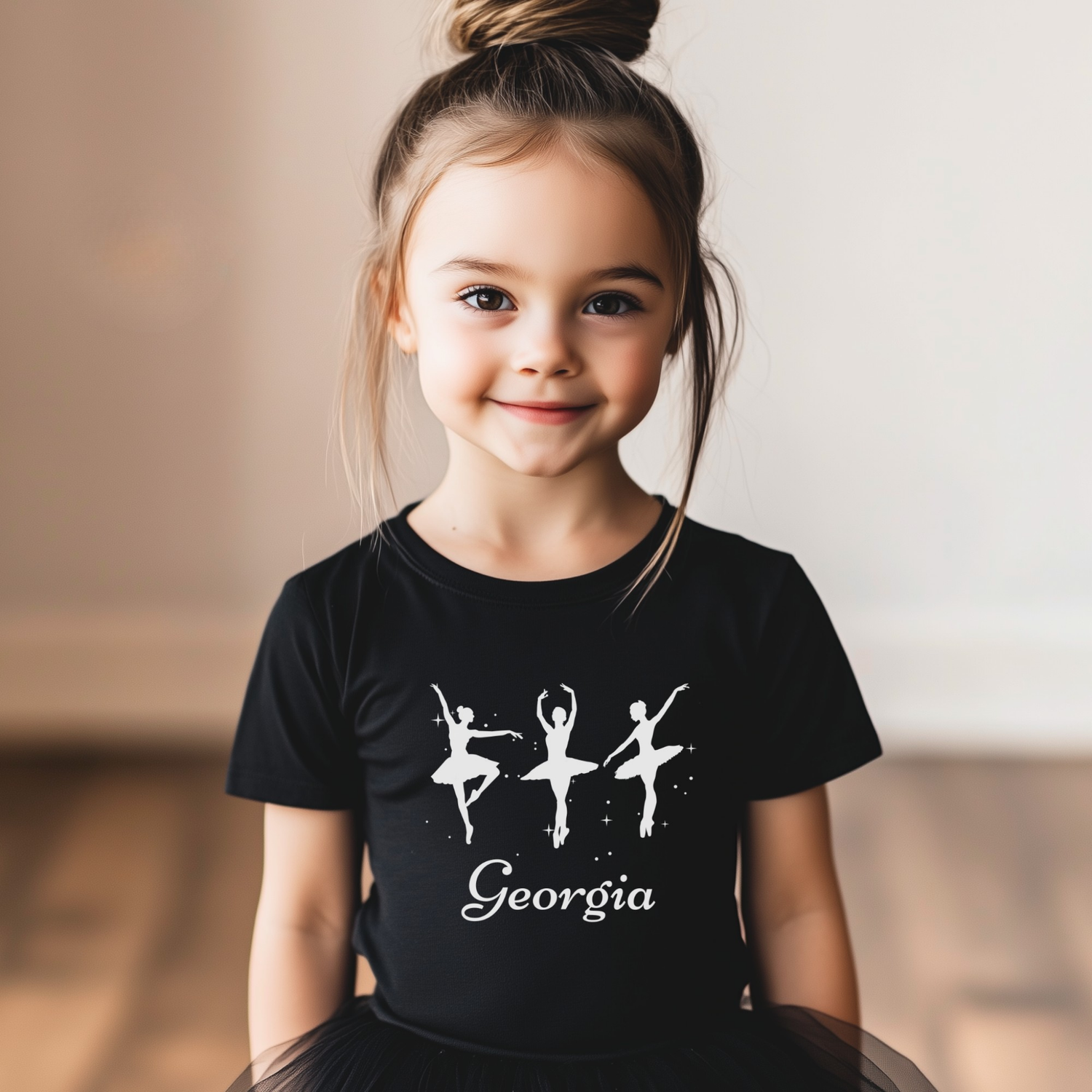 Little girl wearing a black personalised ballet t-shirt with three white ballerina silhouettes and the name “Georgia” printed beneath the design, ideal for young dancers aged 3–13.