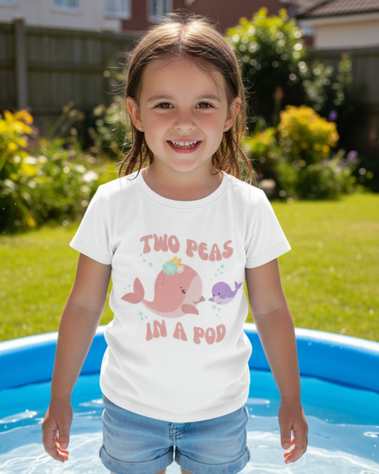 Little girl wearing white Two Peas in a Pod whale print children’s t-shirt and denim shorts standing in paddling pool in sunny garden