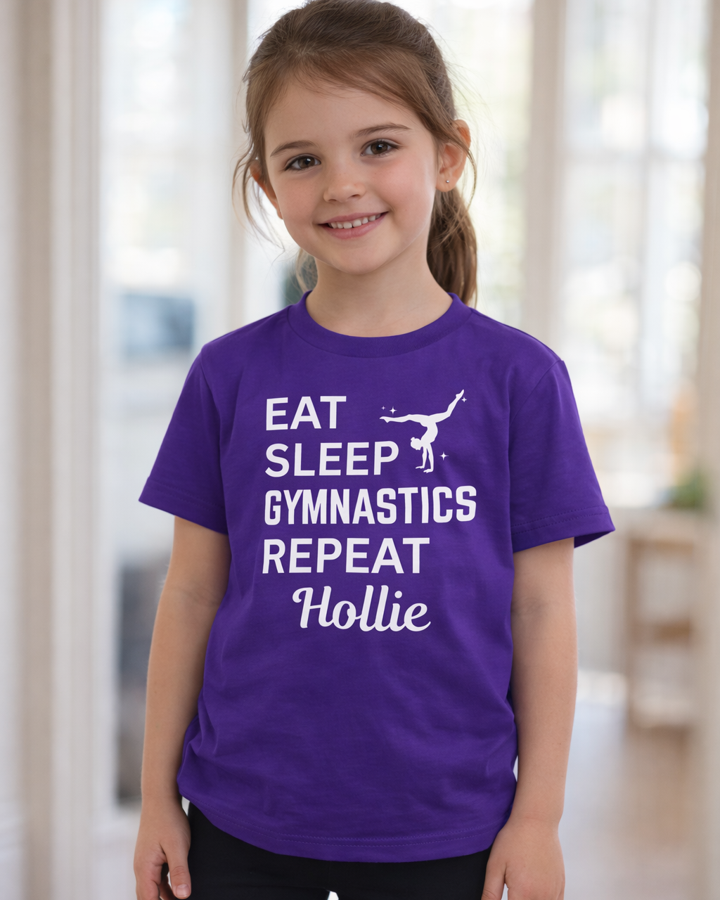 Girl wearing purple personalised “Eat Sleep Gymnastics Repeat” t-shirt with custom name Hollie, kids gymnastics shirt front view