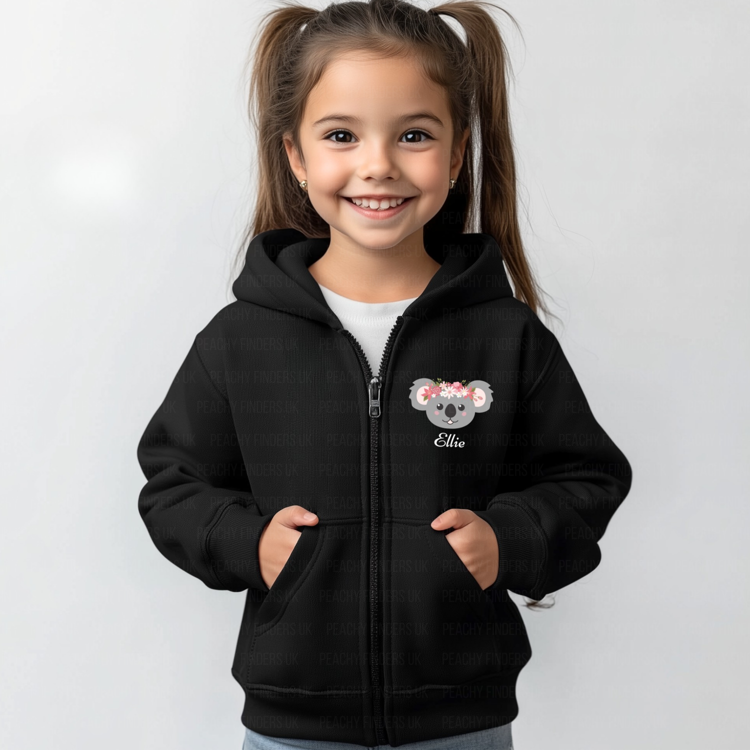 A girl wearing a black zip hoodie with a floral koala motif on the front left side, standing with hands in pockets. The hoodie has the name 'Olivia' printed on under the koala's face.