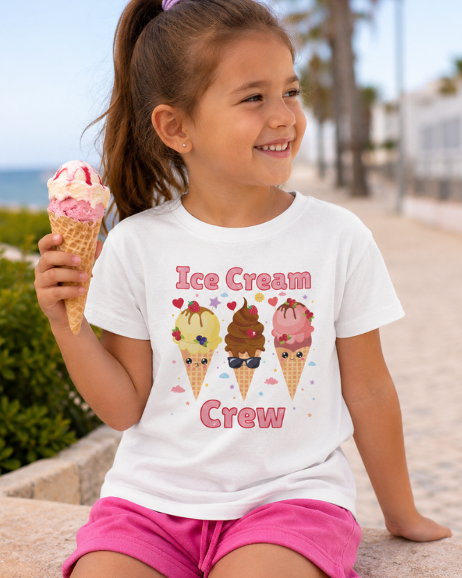 Young girl holding an ice cream cone wearing a 'Ice Cream Crew' t-shirt by the beach.
