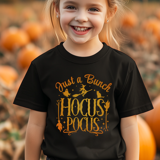 Smiling young girl wearing a black Halloween t-shirt with the phrase “Just a Bunch of Hocus Pocus” in ombre orange, standing in a pumpkin patch.