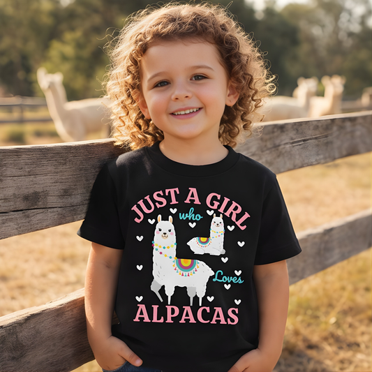 Smiling girl wearing black “Just A Girl Who Loves Alpacas” t-shirt with alpaca farm in the background