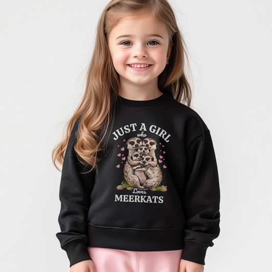 Girl wears a black sweatshirt with “Just a Girl Who Loves Meerkats” text and cute meerkat family graphic surrounded by pink hearts.