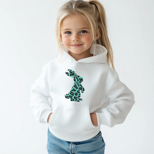 Blonde child in white hoodie with teal and black leopard print bunny graphic, hands in pockets.