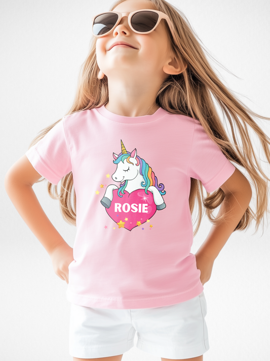 Girl wearing personalised light pink unicorn heart T-shirt with custom name print, kids magical unicorn top.