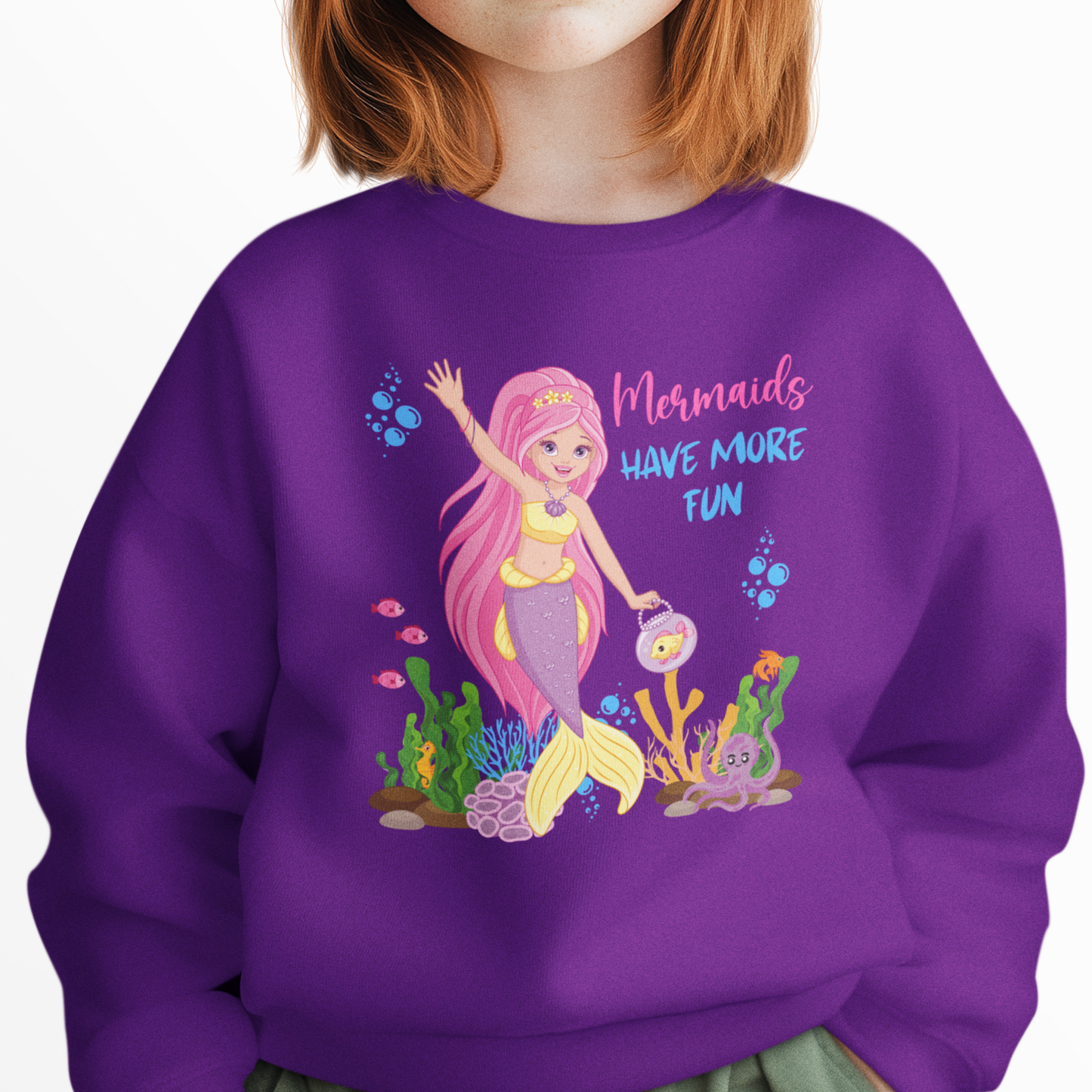Girl wearing a purple sweatshirt featuring a pink-haired mermaid with the text “Mermaids Have More Fun” surrounded by underwater sea creatures.
