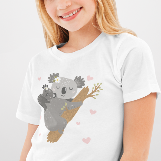 Young girl wearing a white graphic tee featuring an illustration of a mother koala cuddling her baby while clinging to a tree, surrounded by small pink hearts and flowers.