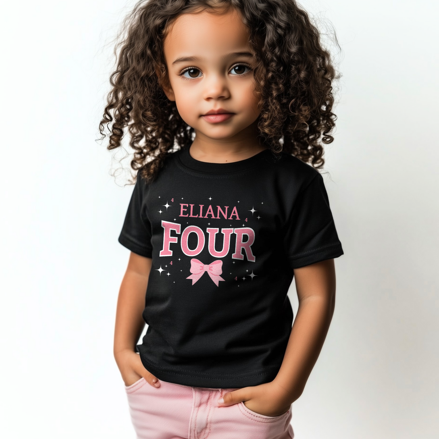 Little girl wearing a black personalised “Four” birthday t-shirt with pink bow and stars, hands in pockets.