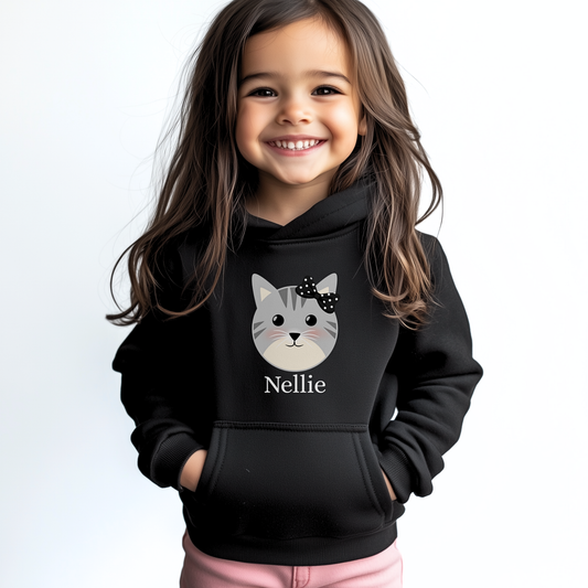 Little girl wearing personalised black cat hoodie with custom name ‘Nellie’ printed under a grey kitten face and black polka-dot bow