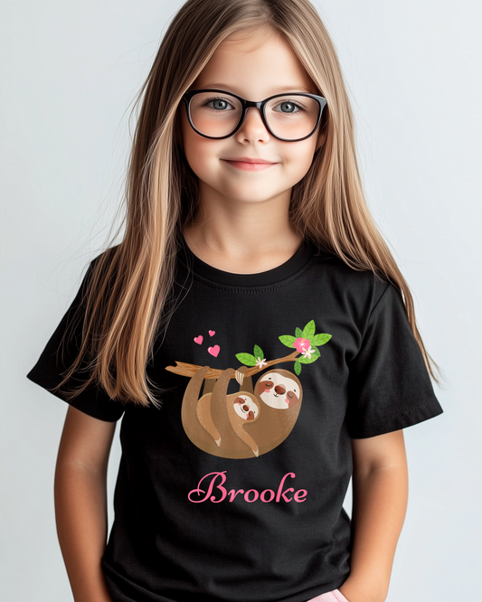 Young girl with long hair and glasses wearing a black T-shirt with a cute mum and baby sloth hanging from a leafy branch with pink hearts and flowers, and the name “Brooke” printed in pink script.