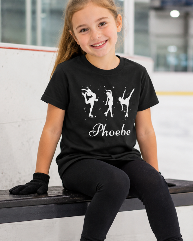 Young girl wearing a black t-shirt with ice-skaters illustrations custom name 'Phoebe' text, sitting on an ice rink bench.