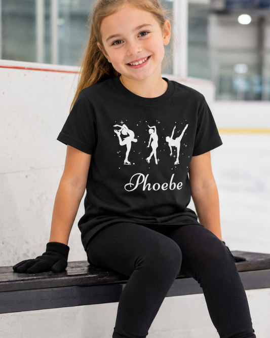 Young girl wearing a black t-shirt with ice-skaters illustrations custom name 'Phoebe' text, sitting on an ice rink bench.