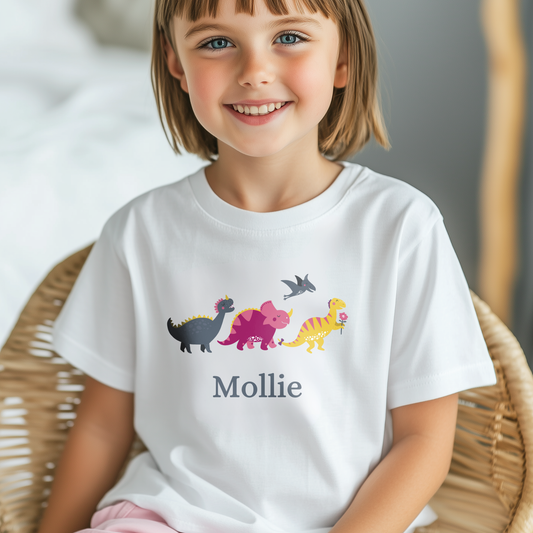 Young girl wearing a white personalised dinosaur t-shirt featuring colourful cartoon dinosaurs and the name "Mollie" printed below.