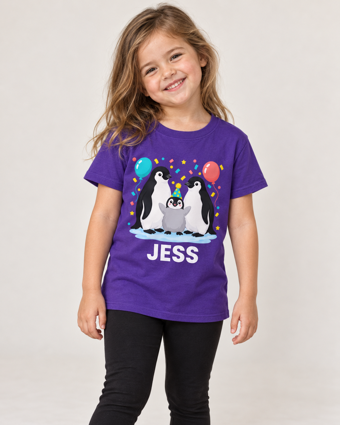 Girl wearing a purple birthday penguin T-shirt with Jess beneath the balloon and confetti design, styled with black leggings in a bright studio.