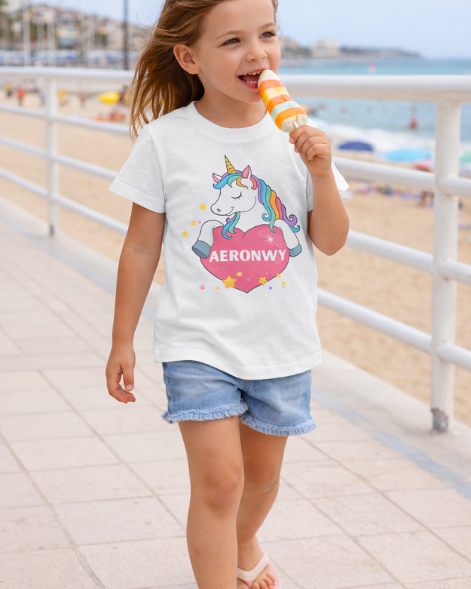 Young girl wearing a white t-shirt with a unicorn design with her name featuring inside the large pink heart -walking on a beach boardwalk.