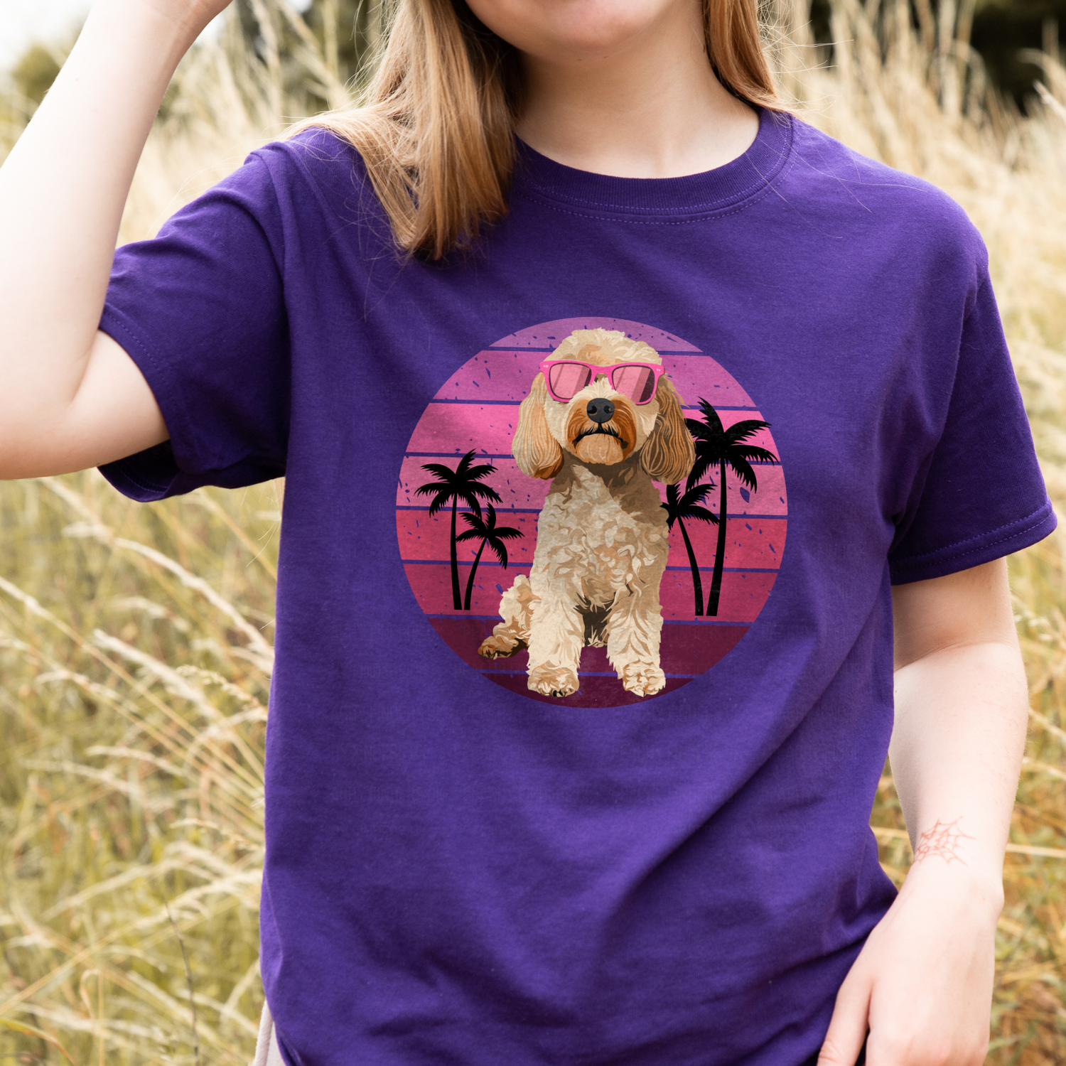 Girl wearing a purple t-shirt featuring a summer cockapoo dog graphic with pink sunglasses and palm trees, photographed outdoors.