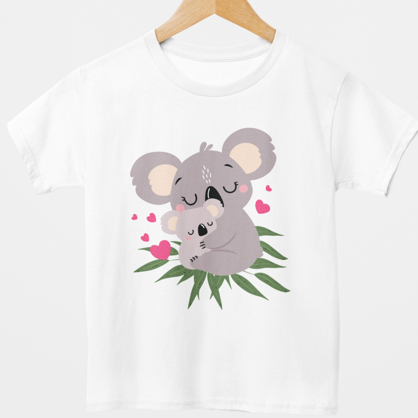 Girls white cotton t-shirt styled on a wooden hanger featuring a cute baby and mum koala embracing with scattered pink hearts and green eucalyptus leaves