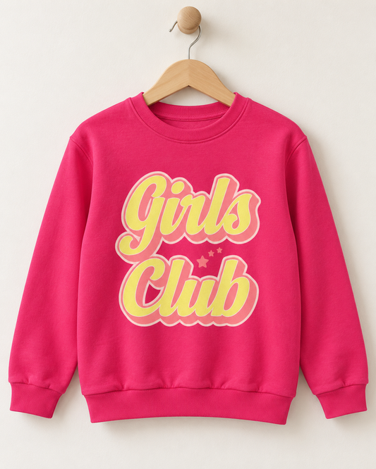 A kids bright pink crewneck sweatshirt hanging on a wooden hanger against a light beige wall. The sweatshirt features a retro-style graphic on the front reading 'Girls Club' in yellow with a pink outline.