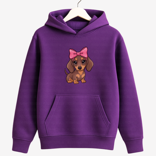 Kids purple hoodie with a cartoon dachshund wearing a pink bow graphic on a wooden hanger