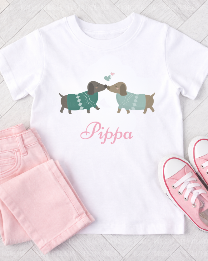 Girls white t-shirt with dachshund design and 'Pippa' text, paired with pink shorts and shoes on a light wooden floor.