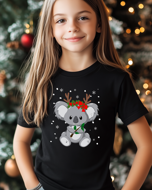 Girl standing in front of a Christmas tree wearing a festive koala black printed t-shirt.