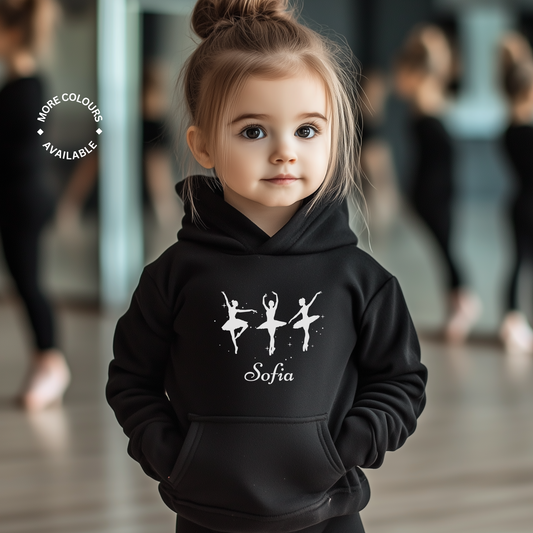 Little girl modelling a black hoodie featuring three elegant ballerina silhouettes printed on the front, with a custom-name underneath