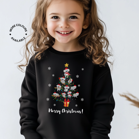Smiling girl wearing a black Christmas sweatshirt featuring a Christmas tree made of koalas in Santa hats with fairy lights and snowflakes.