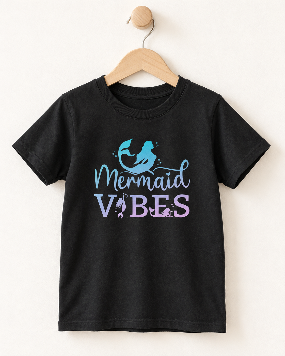Black short sleeve girls’ Mermaid Vibes T-shirt with blue and lilac ombre mermaid design displayed on a wooden hanger