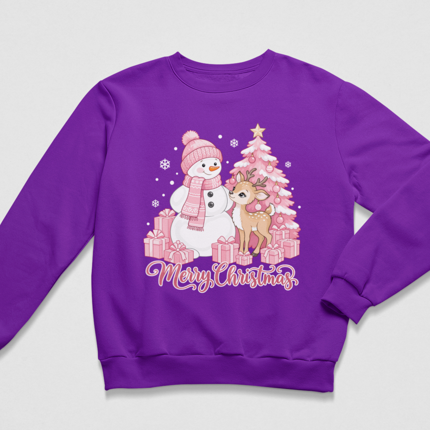 Flat lay of a purple kids' Christmas crewneck sweatshirt with a pink graphic of a snowman, a small deer, a decorated pink Christmas tree surrounded by wrapped presents, and the script text "Merry Christmas"